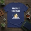 Practice Gratitude text design on a navy t-shirt with a sun, plant, and birds graphic
