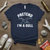 Navy blue t-shirt with white text "PRETEND I'M A GULL" and a graphic of a flying seagull over waves