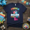 Navy blue t-shirt with "Prima Shark Itzayana 1" text, featuring a cartoon shark wearing sunglasses and holding a cupcake, designed