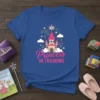 Blue t-shirt with "Princess IN TRAINING" text and a cartoon castle graphic with a crown, stars, and clouds