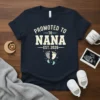 Promoted to Nana Est. 2026 text with baby footprints graphic on a navy t-shirt