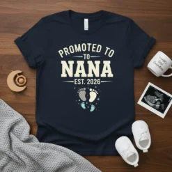 Promoted to Nana Est. 2026 text with baby footprints graphic on a navy t-shirt