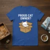 Proud Cat Owner? text above a cute white cat peeking out of a cardboard box on a blue t-shirt design