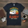 Proud New Daddy Est. 2022 t-shirt with a hand holding a baby's foot and a retro sunset graphic