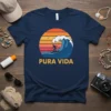 Pura Vida text with a surfer riding a wave against a retro sunset graphic on a navy t-shirt