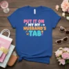 Blue t-shirt with bold text "PUT IT ON MY MY HUSBAND'S TAB" in pink, orange, and teal, featuring shopping-related icons