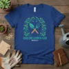 Blue t-shirt with green leafy wreath framing gardening tools and text "QUILCENE GARDEN CLUB BRINNON"