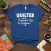Blue t-shirt with "QUILTER Promoted to Customer" text, scissors, thread, and stacked fabric graphics
