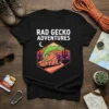 Rad Gecko Adventures text above a green gecko on a rock in a desert landscape design on a black t-shirt