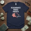 Reaganomics Ruined America text on a navy t-shirt with a cracked piggy bank and downward economic graph