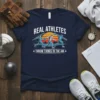 Navy t-shirt with "Real Athletes Throw Things In The Air" text and graphic of athletes throwing javelin, shot put, and