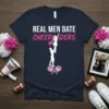 Real Men Date Cheerleaders quote with graphic of a male base lifting a female cheerleader, on a navy t-shirt