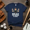 Navy t-shirt with cartoon umpire and text "RELAX THE UMPIRE IS HERE"