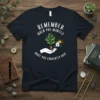 Remember When You Wanted What You Currently Have quote on a navy t-shirt with a hand holding a sprouting plant