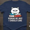Grumpy cat sitting on books with text "Remind Me Why I Should Care" on a navy blue t-shirt