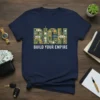 RICH BUILD YOUR EMPIRE text design on navy t-shirt, featuring money and city graphics within the word RICH