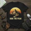 Ride The Peak mountain biking t-shirt with a cyclist on a winding trail against a sunset mountain backdrop