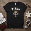 Black t-shirt with "RISEN" text above a mountain and cross graphic, symbolizing Easter and Christian faith