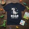 Kids t-shirt with "ROAR SOME MORE!" text and a cute grey dinosaur graphic surrounded by stars and comets