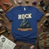 Blue t-shirt with the word ROCK in cream letters above a gray crystal formation illustration, designed for geology lovers