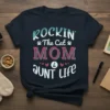 Rockin' The Cat Mom & Aunt Life text design with decorative elements and paw prints on a navy t-shirt