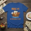 T-shirt with "RULE #1 BE PREPARED TO EAT" text and a pirate ship filled with food, orange lettering, cartoon style