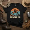Saddle Up text with cowboy riding horse graphic and retro sunset design on a black t-shirt