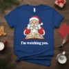Santa Claus with spectacles reading a book titled "Nice" and "Naughty" with text "I'm watching you" on a blue t-shirt