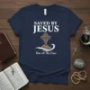 Saved By Jesus Rise At The Cross t-shirt with a wooden cross on a rocky hill and waves below