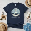 Navy blue t-shirt with a circular design featuring palm trees, ocean, and sunset, text reads SEASIDE 30A, inspired by coastal