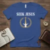 Blue t-shirt with white text "SEEK JESUS" above a golden laurel wreath surrounding a white figure reaching towards a golden