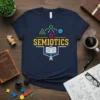 Navy t-shirt with the word SEMIOTICS in yellow, surrounded by colorful icons representing communication and learning, including an open book