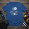 SENIOR 2027 text with a graphic volleyball in motion, white outline on a blue t-shirt