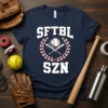 SFTBL SZN graphic tee featuring crossed baseball bats, a softball, and a laurel wreath on a navy blue shirt