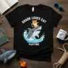 Shark Loves Cat Playtime t-shirt design featuring a cartoon cat riding a shark in waves, with playful text