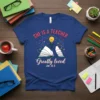 Teacher appreciation t-shirt with text "SHE IS A TEACHER Greatly loved Jer 31:3" and an illustration of an open book