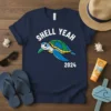 Navy blue t-shirt with white text "SHELL YEAH 2024" and a cartoon turtle graphic