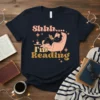 Shhh..... I'm Reading quote on a navy t-shirt, featuring a person reading in a chair with coffee and stars