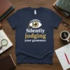 Navy t-shirt with white and gold text "Silently Judging Your Grammar" and an eye graphic with a magnifying glass