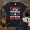 Singing Is The Heartbeat Of My Life text design with microphone, hearts, and musical notes graphic on a navy t-shirt