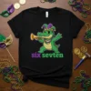 Cartoon alligator wearing a jester hat and beads, playing a trumpet with "six sevten" text below, on a black t-shirt
