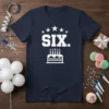 Navy blue t-shirt with white text "SIX." and a birthday cake graphic with five candles, surrounded by stars