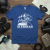 SLEDHEAD text with a snowmobile rider on a mountain slope, white graphic design on a blue t-shirt