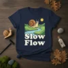 Slow Flow t-shirt design with a cartoon snail on a winding river path under a sunny sky