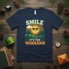 Smile It's The Weekend t-shirt with a smiling sun wearing sunglasses and a forest landscape graphic