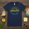 Navy blue t-shirt with yellow "smile" text and sun graphic, and a teal smile graphic