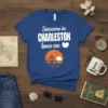 Blue t-shirt with white text "Someone in Charleston loves me" and a sunset bridge graphic, representing Charleston SC love