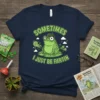 Navy t-shirt with "Sometimes I Just Be Fartin" text above a cartoon frog on a lily pad, featuring green cartoon