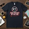 Dark navy t-shirt featuring the text "SORRY FOR WHAT MY FACE SAID" inside a red speech bubble, with a cartoon