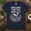 Spilling The Tea Since 1773 quote on a navy t-shirt with a vintage teapot pouring into teacups graphic
